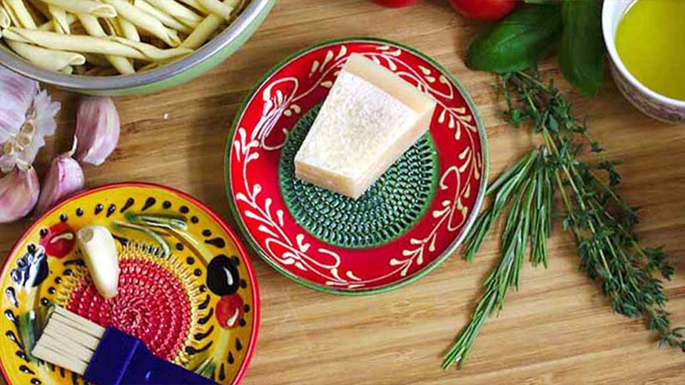 Käse auf buntem Teller mit Kräutern, Knoblauch, Olivenöl und Gemüse auf Holztisch. Zutaten für italienische Küche. Rezeptvorbereitung mit Pasta und frischen Zutaten. Kulinarische Szene mit Lebensmittelzubehör.